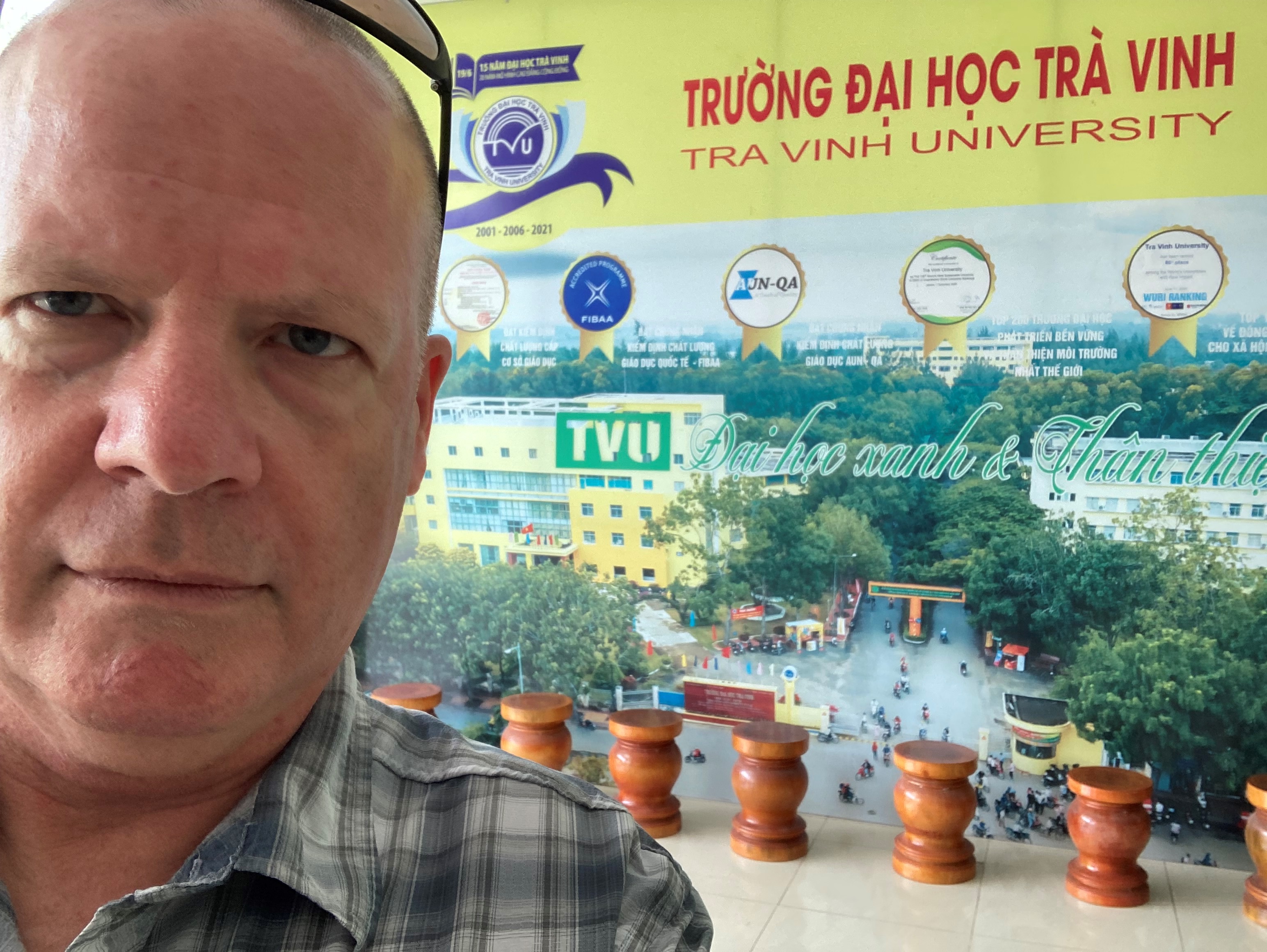 David Harvey in front of a poster of Tra Vinh University campus.